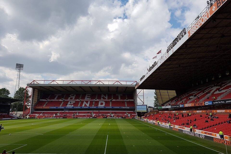 A football stadium with red seating and a large digital screen.
