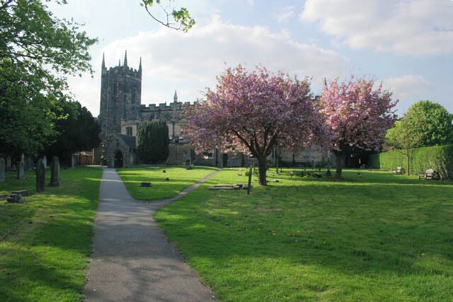 Un sentier menant à une église dotée d’un clocher, entourée d’herbe verte et d’arbres en fleurs.