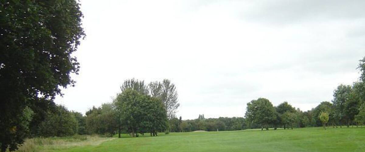 A green golf course with trees and a cloudy sky.
