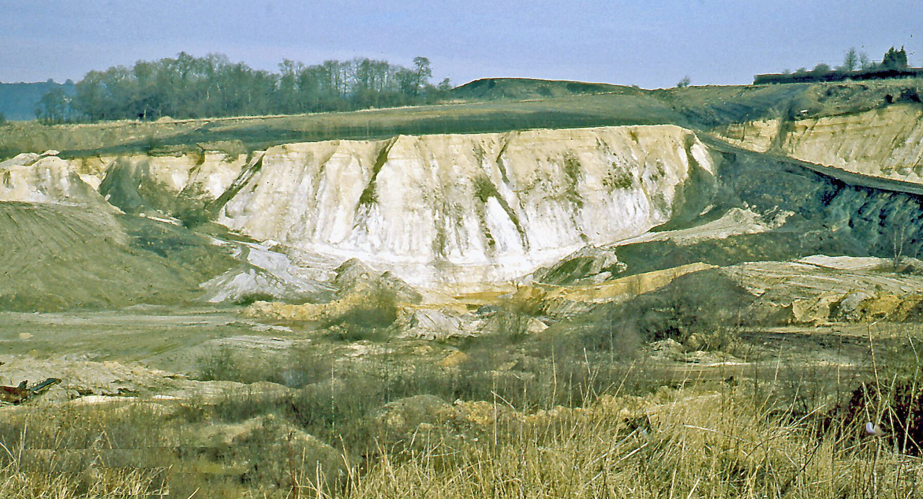 A barren landscape with a large, eroded hill and sparse vegetation.