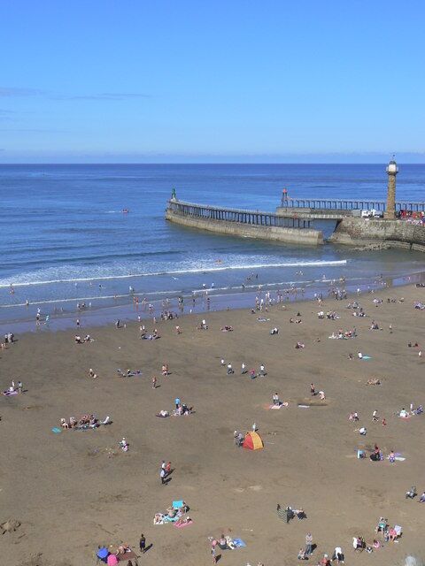 Una playa con gente tomando el sol y un muelle que se adentra en el agua.