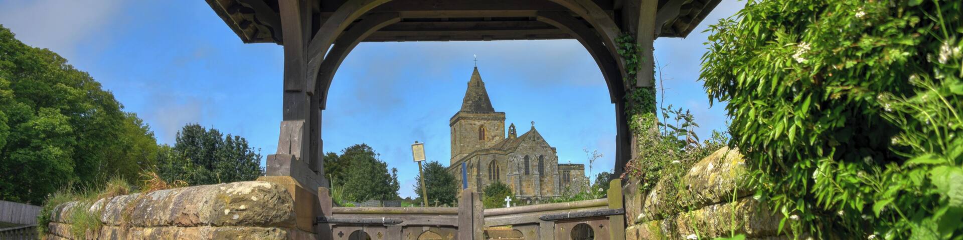 A stone wall with a wooden archway leading to a church.