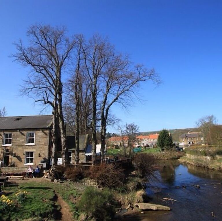 A stone building with a signboard, a river, and leafless trees.