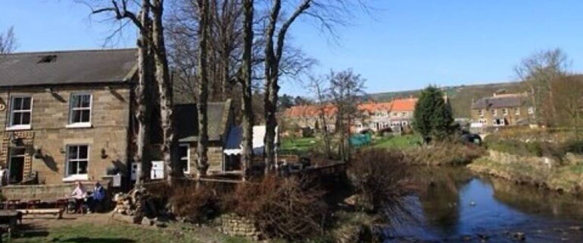 A stone building with a signboard, a river, and leafless trees.