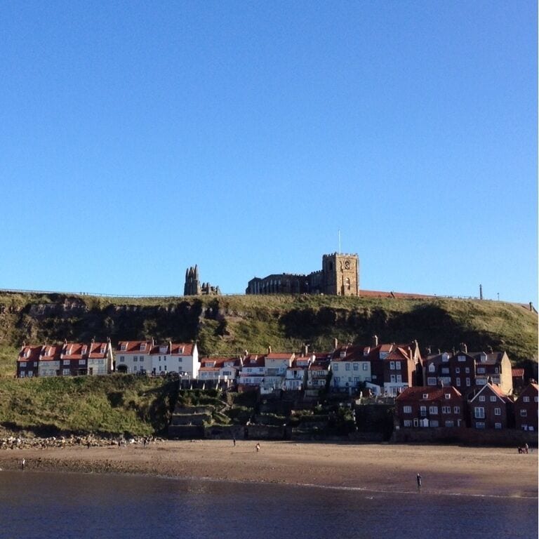 A coastal town with a prominent church on a hill, houses along the shore, and a beach.