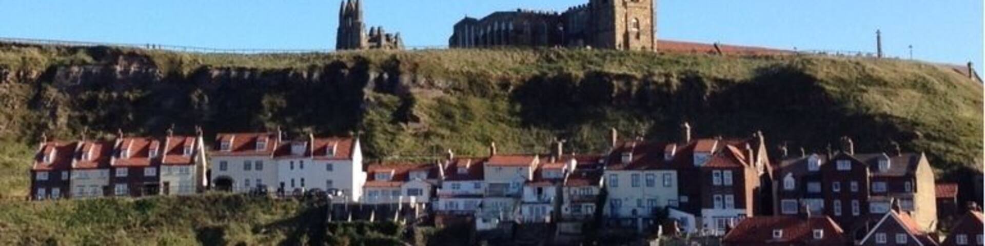 A coastal town with a prominent church on a hill, houses along the shore, and a beach.