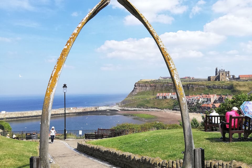 A coastal town with a historic castle, a sea wall, and a metal archway.