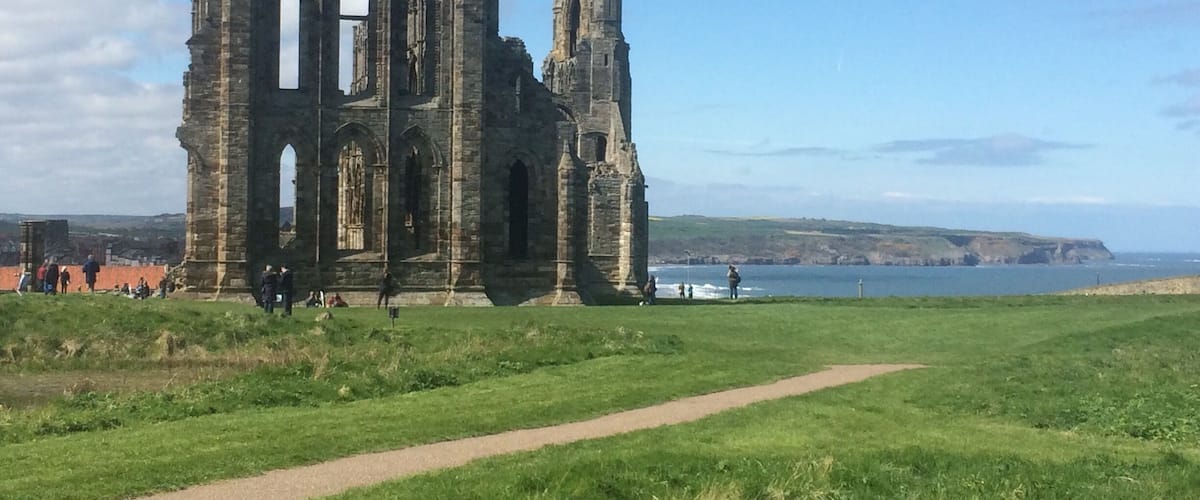 A historic stone ruin with arched windows and a tall spire, set against a coastal backdrop with a clear sky.