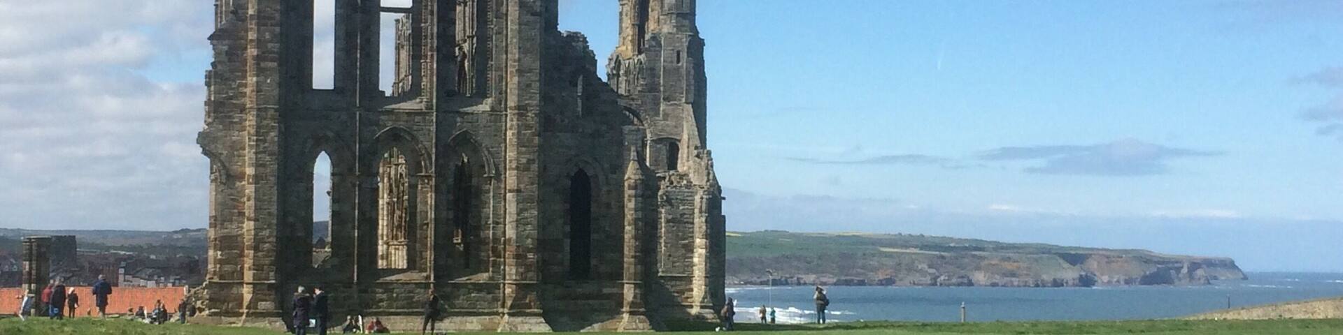 A historic stone ruin with arched windows and a tall spire, set against a coastal backdrop with a clear sky.