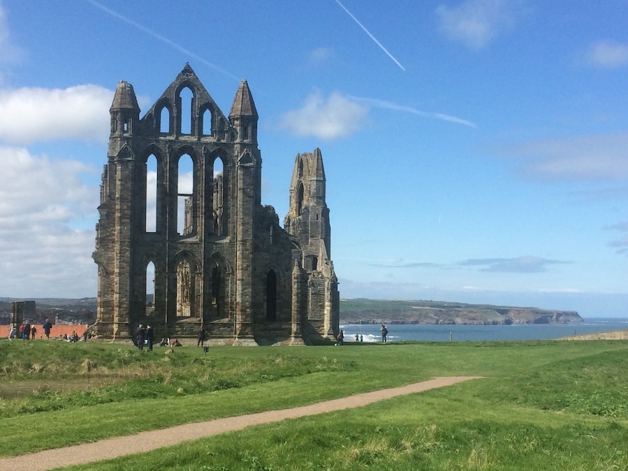 A historic stone ruin with arched windows and a tall spire, set against a coastal backdrop with a clear sky.