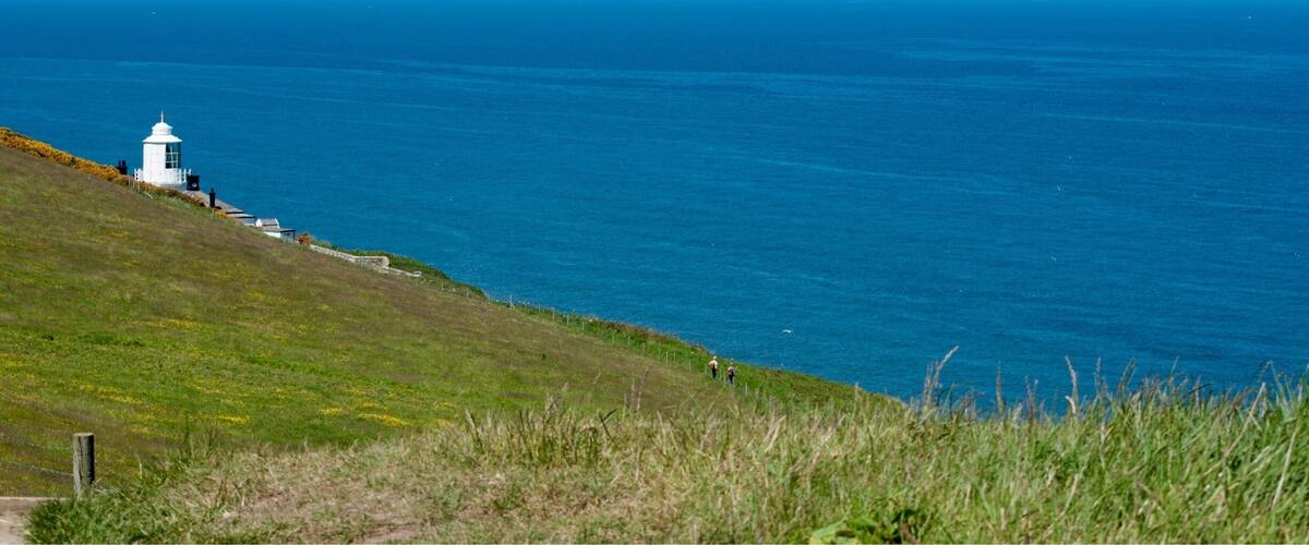 A lighthouse on a grassy hill overlooking the ocean.