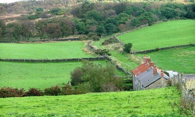 A rural landscape with rolling green fields, stone walls, and a traditional stone house with a red roof.