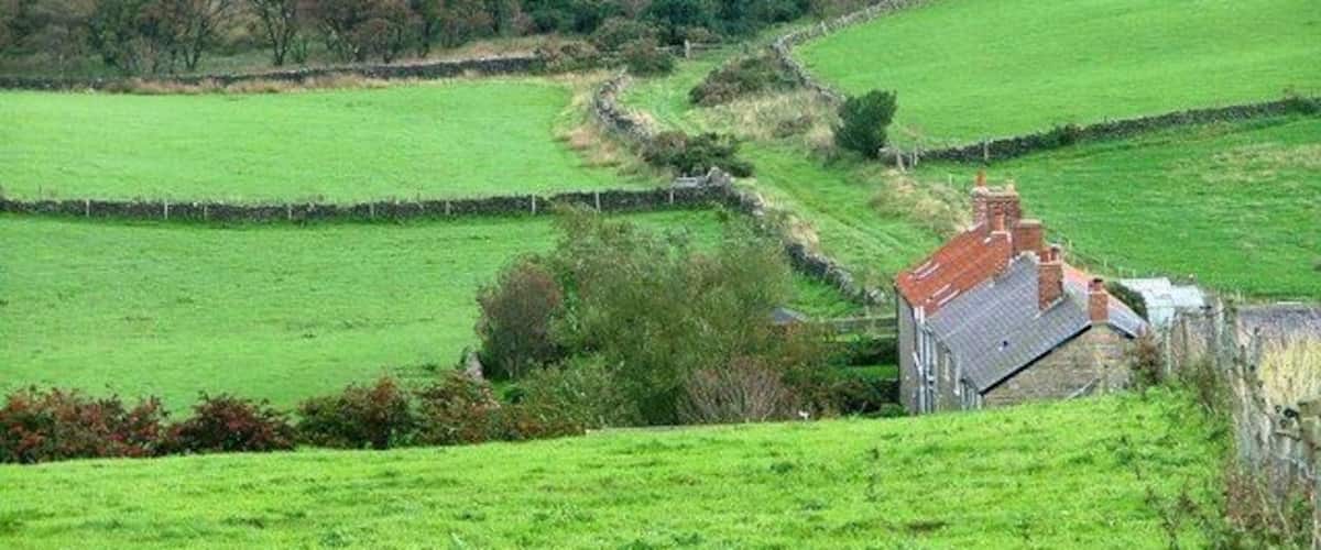 A rural landscape with rolling green fields, stone walls, and a traditional stone house with a red roof.