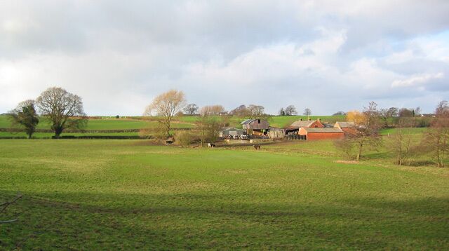 A rural landscape with rolling hills, scattered trees, and farm buildings.