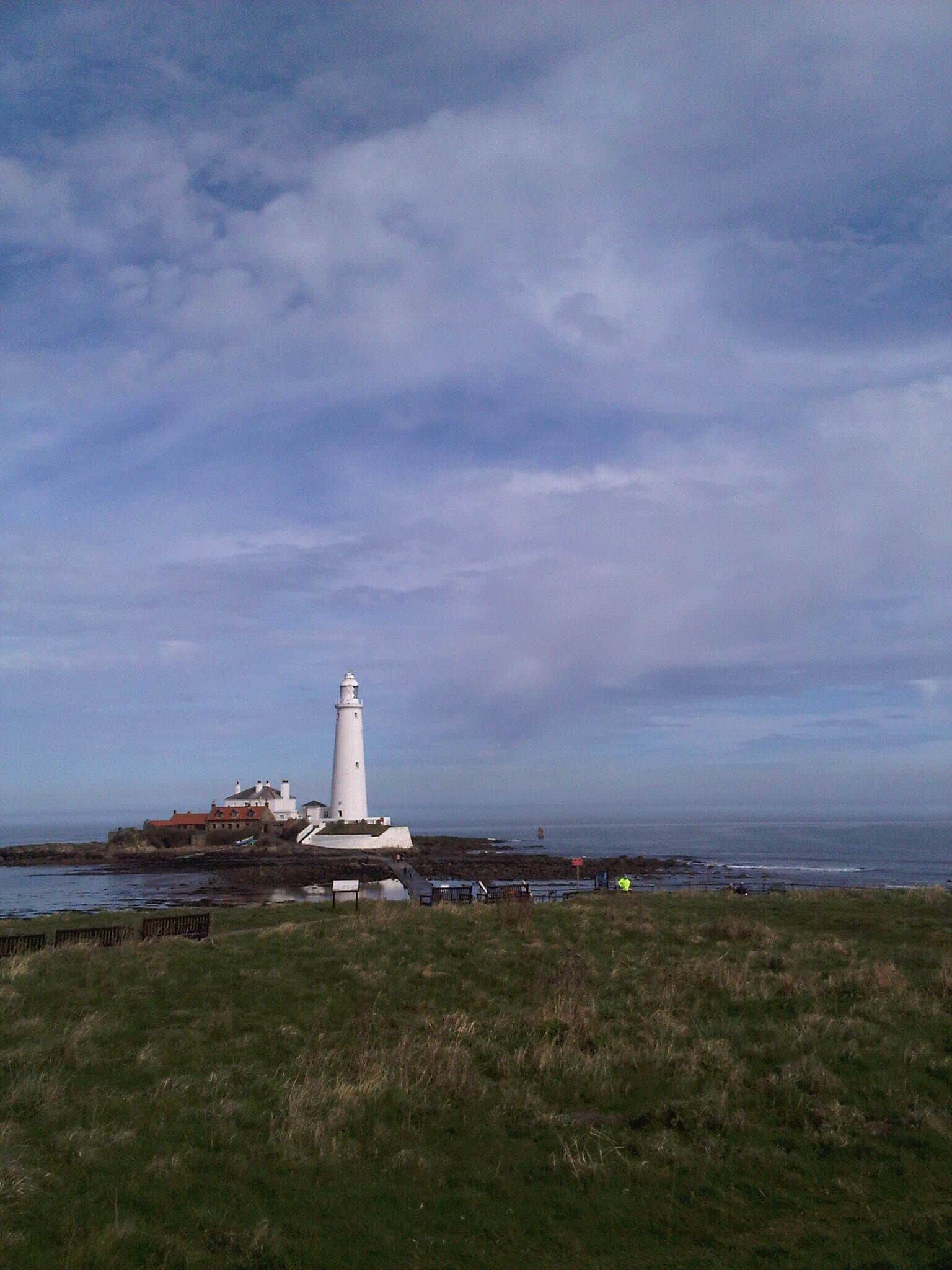 A white lighthouse on a rocky outcrop with a building nearby, overlooking the sea.