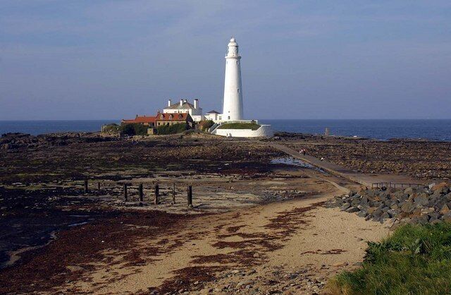 Un faro blanco, una playa y una casa con techo rojo.