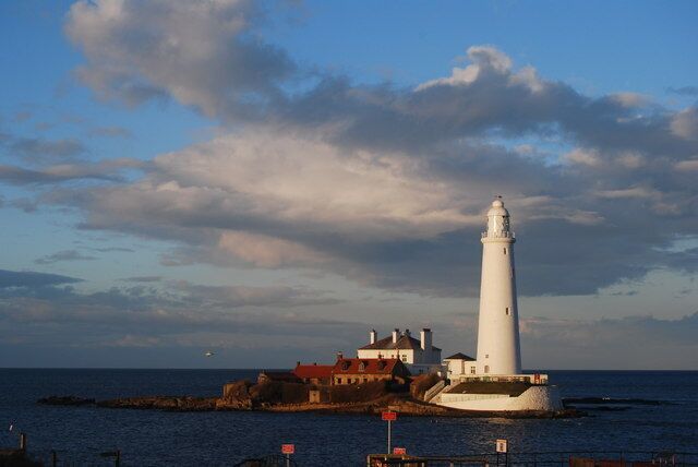 A lighthouse on a rocky outcrop with a red-roofed building nearby.