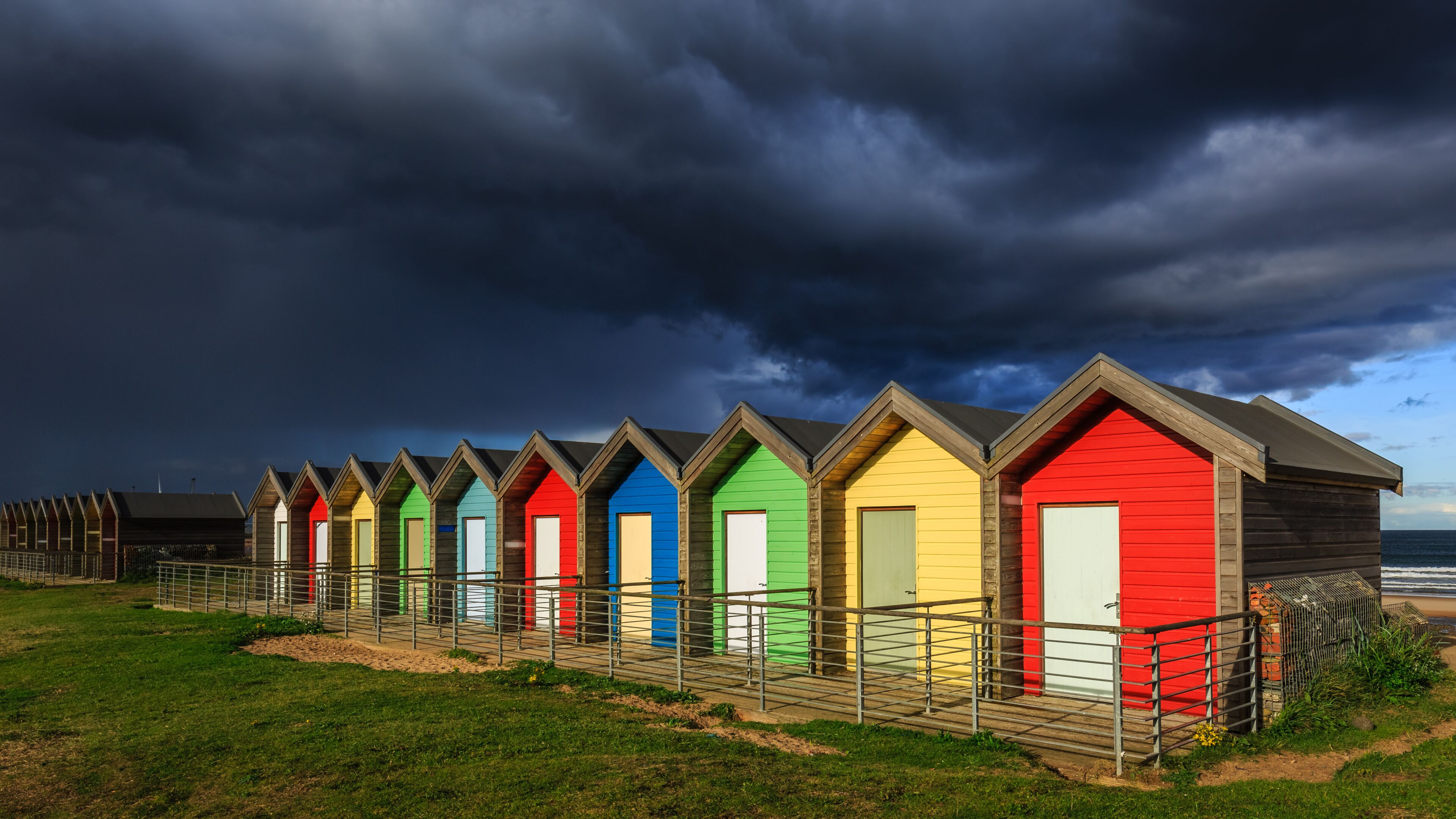 A row of colorful beach huts with a stormy sky in the background.