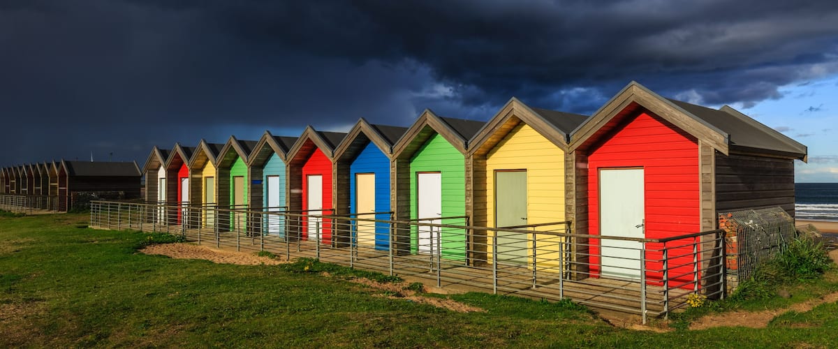 A row of colorful beach huts with a stormy sky in the background.