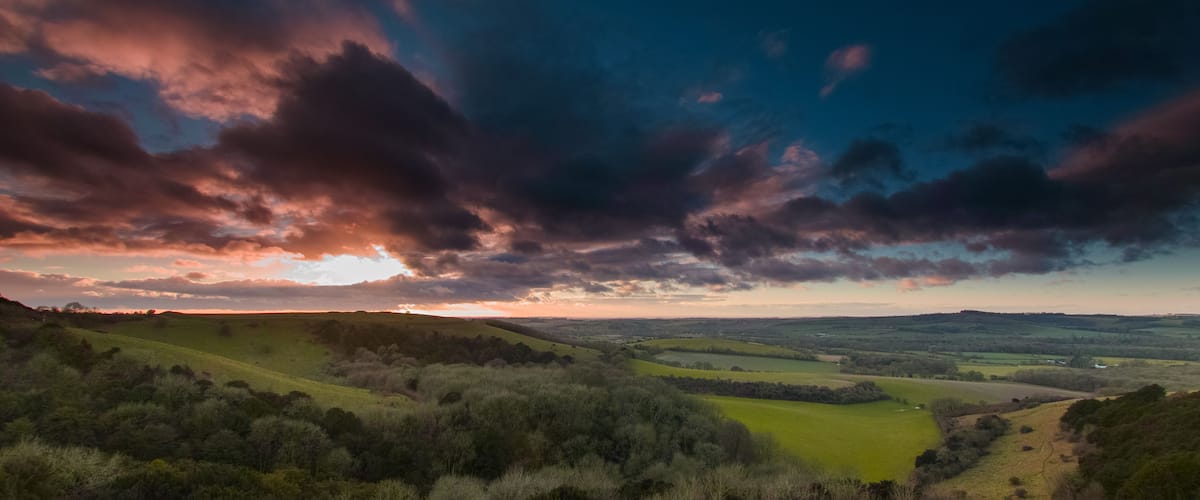Un paysage vallonné, avec des collines douces, une vallée et un ciel spectaculaire parsemé de nuages.