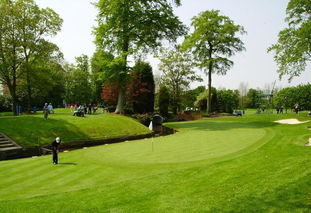 A golf course with a putting green, sand bunkers, and trees.