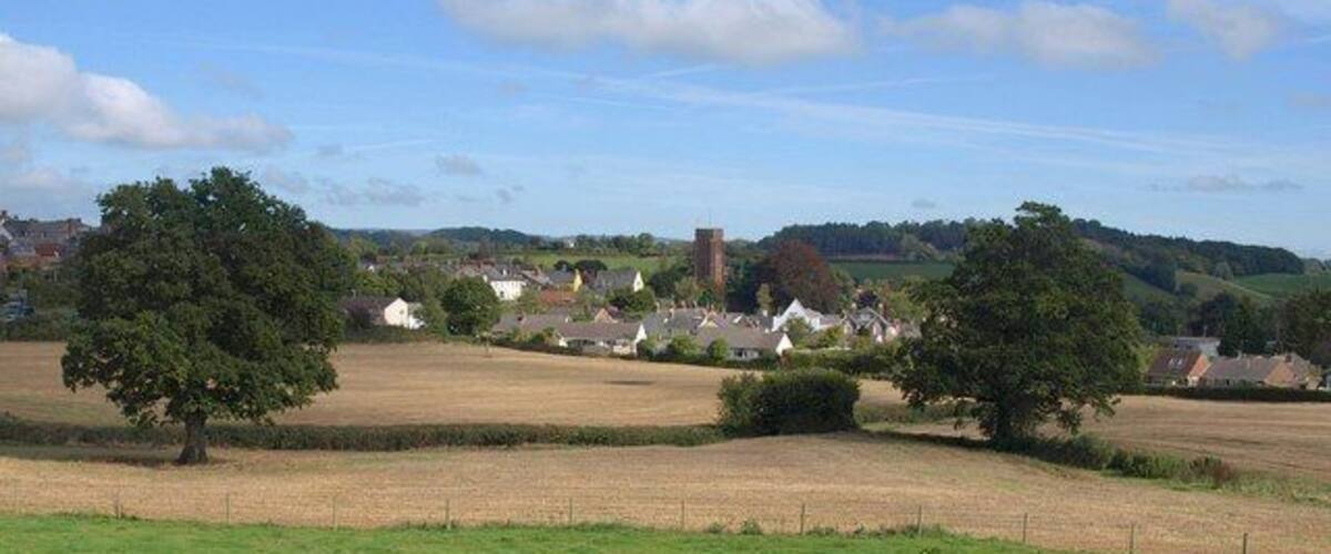 A rural landscape with open fields, scattered trees, and a few houses in the distance.