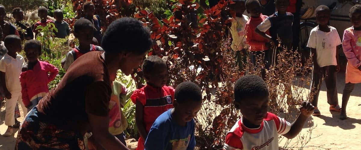 A group of children and adults outdoors, with a woman interacting with a child.