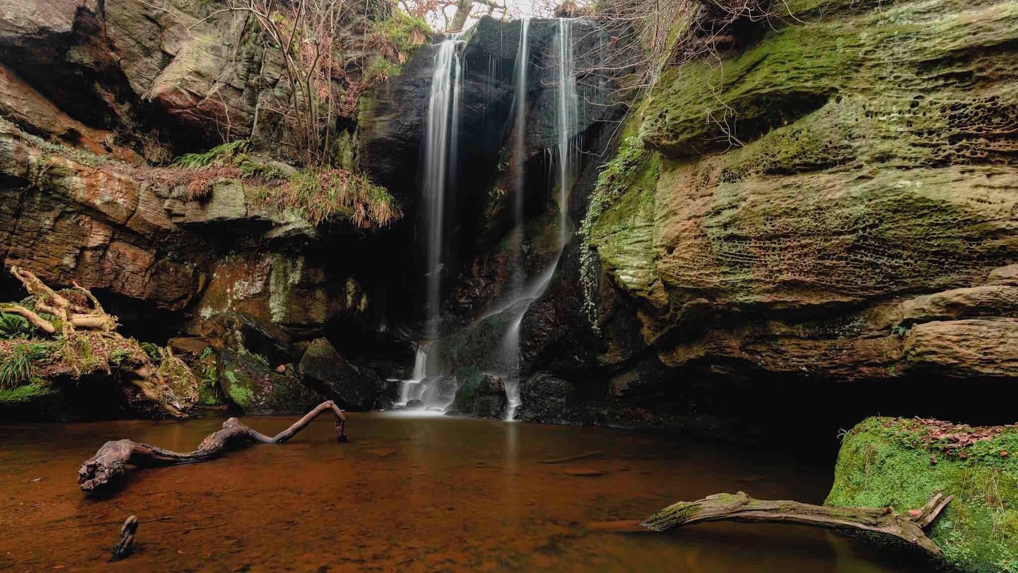 A waterfall cascading into a pool surrounded by moss-covered rocks.