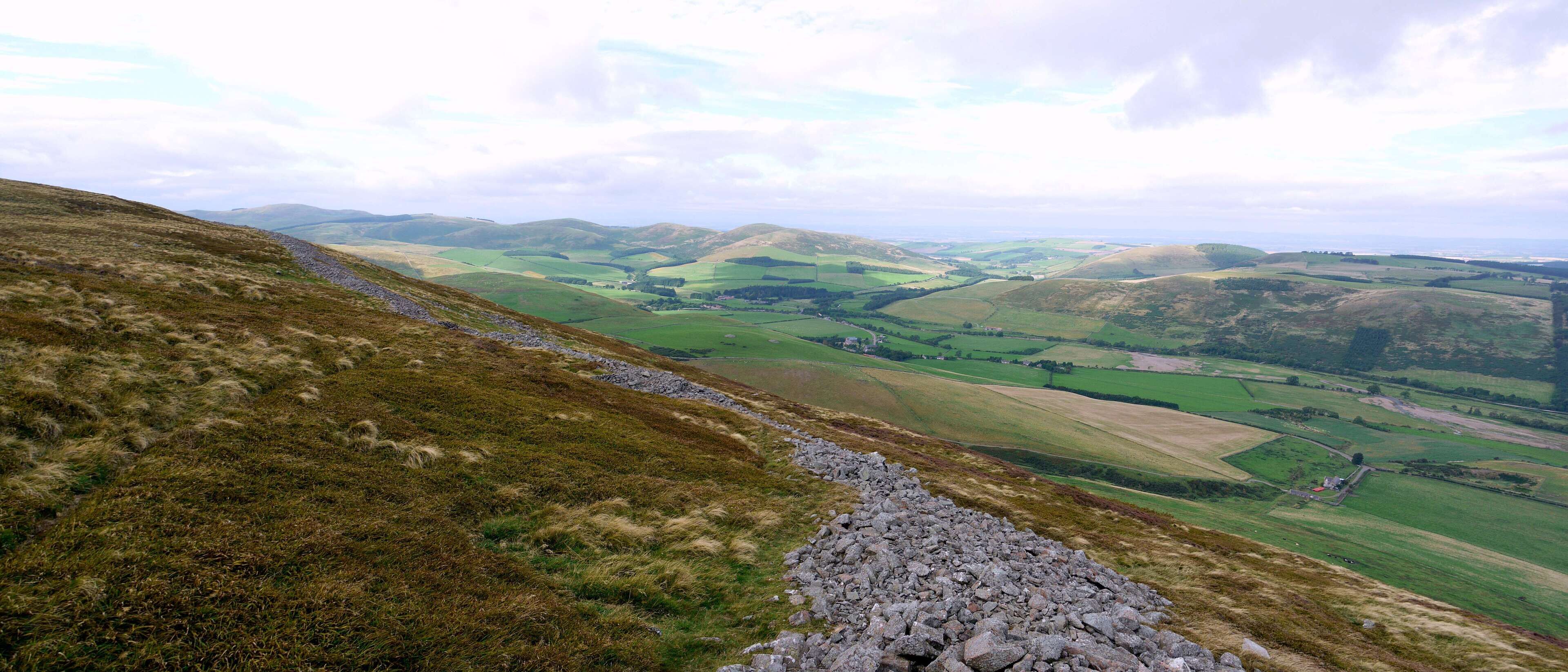 Yeavering Bell hill fort This massive ruined wall encircles the twin tops of Yeavering Bell and encloses a huge area in which the large number of roundhouse remains indicate a sizeable prehistoric population. The view is north-west over the village of Kirknewton and the River Glen valley on its dog-leg between Kilham Hill and Housedon Hill