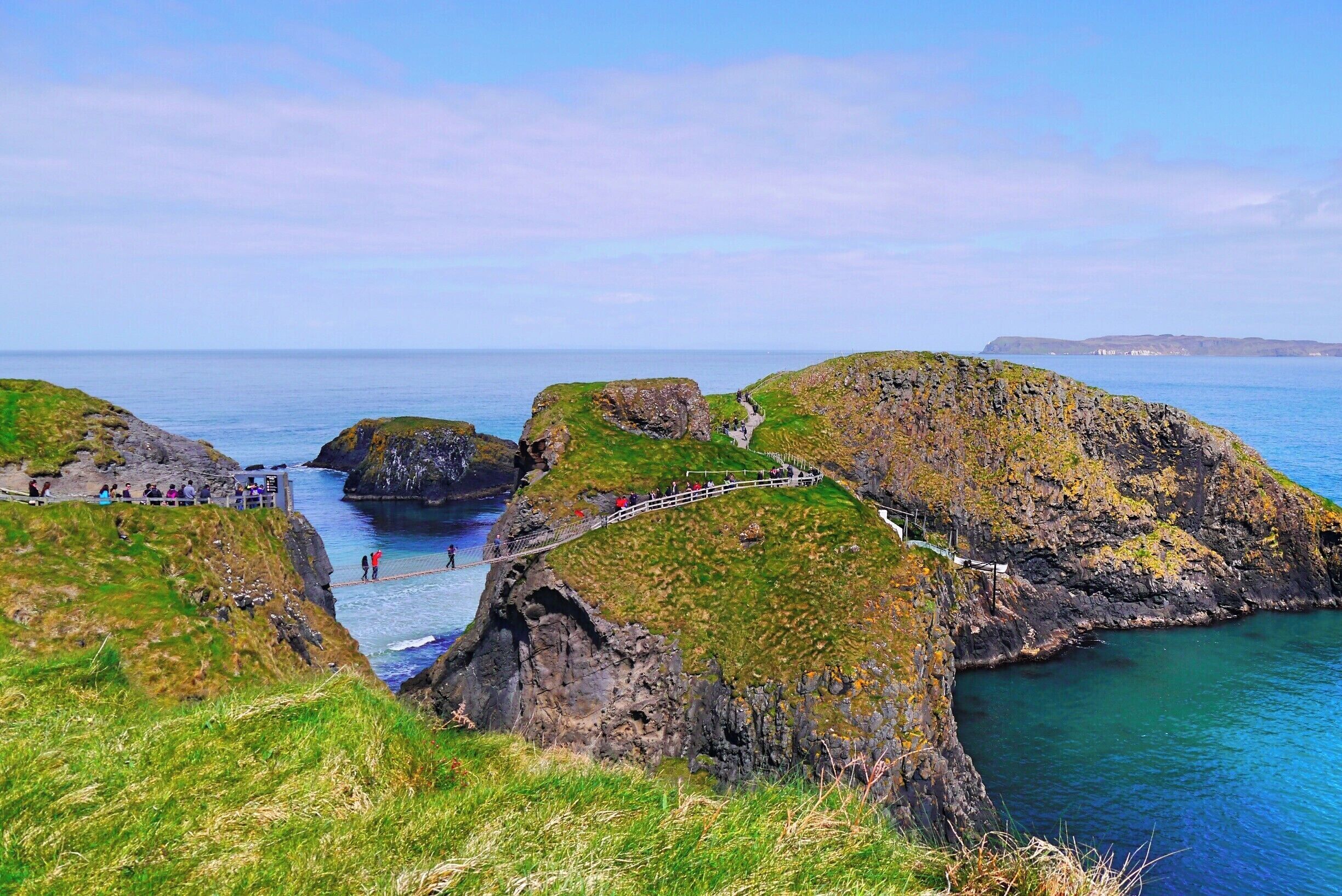 A coastal landscape with rocky cliffs, a narrow sea path, and a clear view of the ocean.