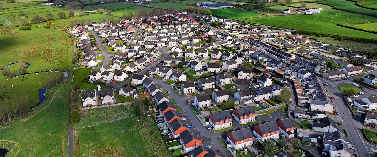 An aerial view of a residential area with houses, roads, and green fields.