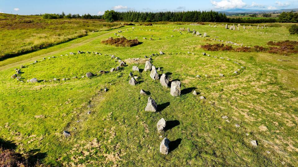 A stone circle in a grassy field with a forest in the background.