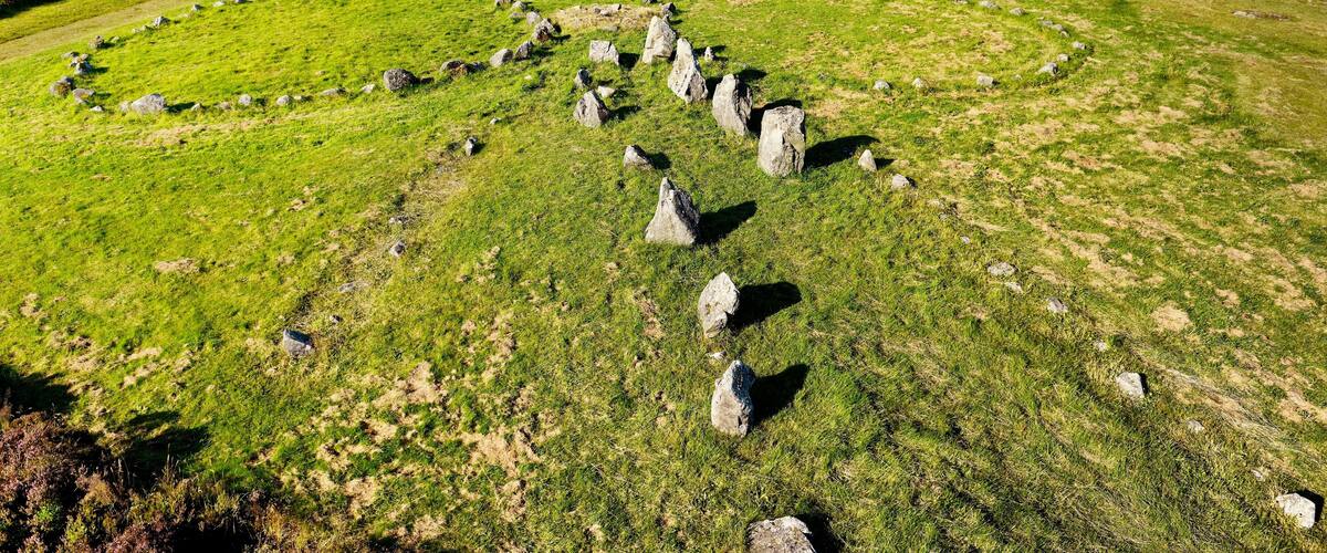 A stone circle in a grassy field with a forest in the background.
