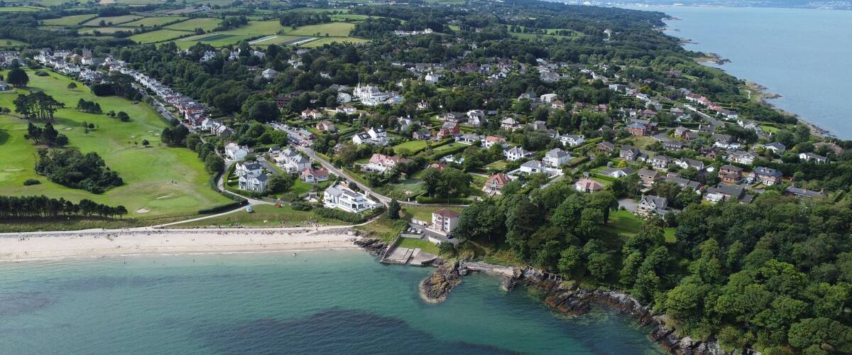 An aerial view of a coastal town with residential areas, a beach, and a rocky coastline.