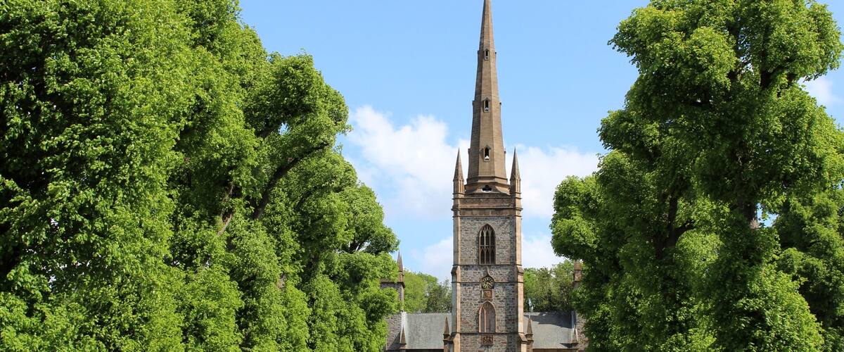 A church with a tall spire, surrounded by lush green trees and a well-maintained lawn.