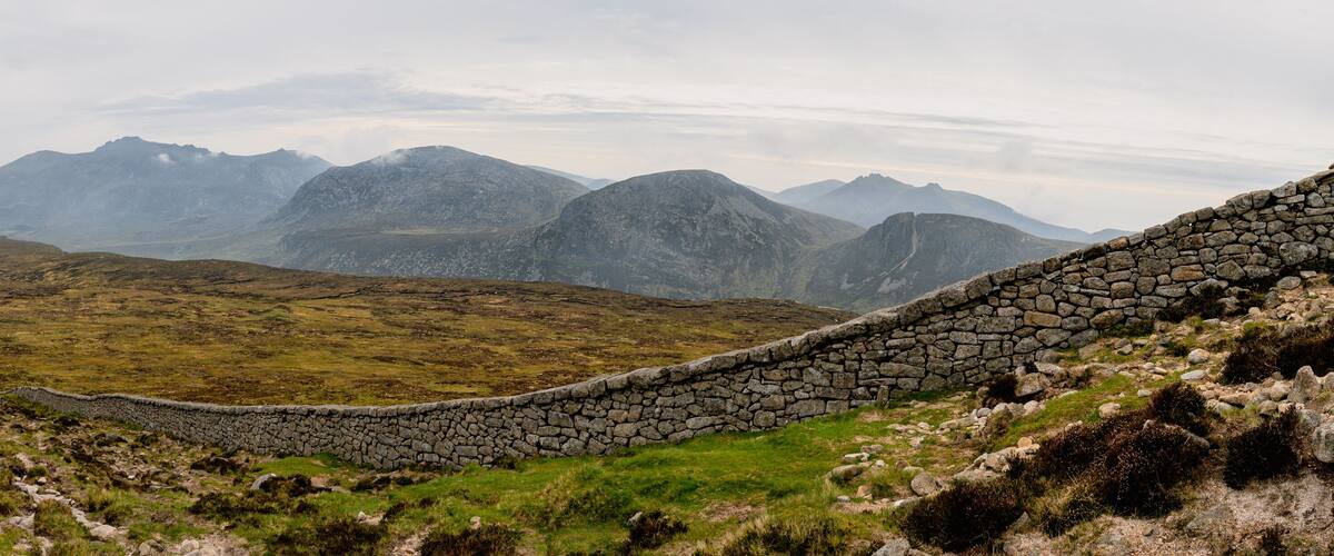 A stone wall winding through a mountainous landscape with green grass and rocky terrain.
