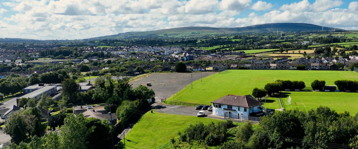 A rural town with a large green field, a blue house, and rolling hills in the background.