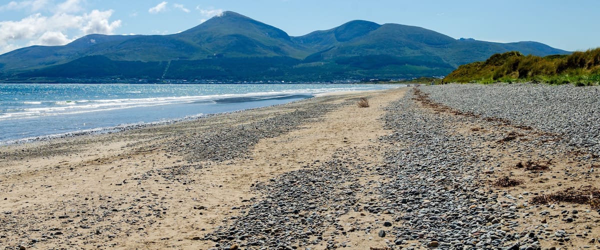 A pebbly beach with mountains in the background.