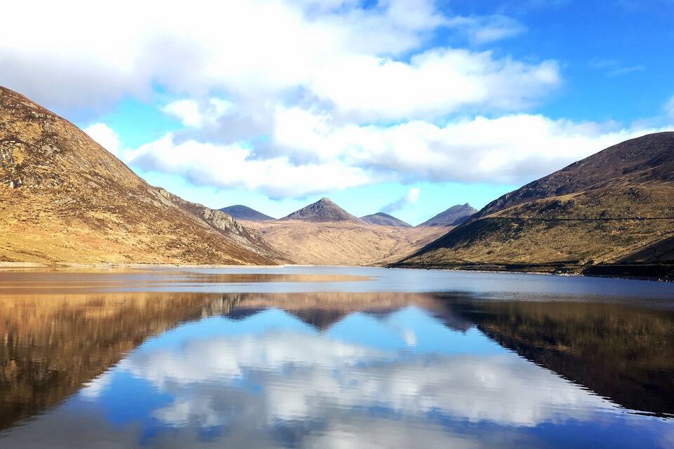 A calm lake reflecting mountains and a partly cloudy sky.