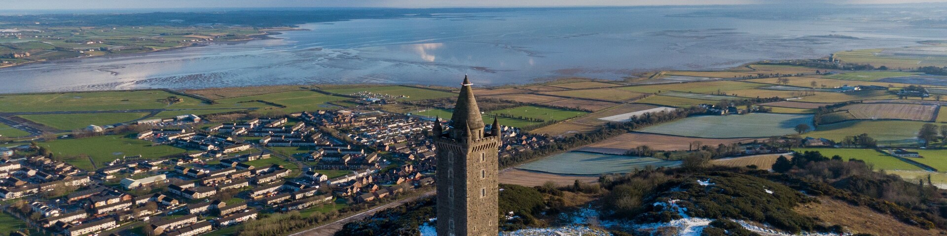 Uma torre medieval, paisagem coberta de neve e um rio.