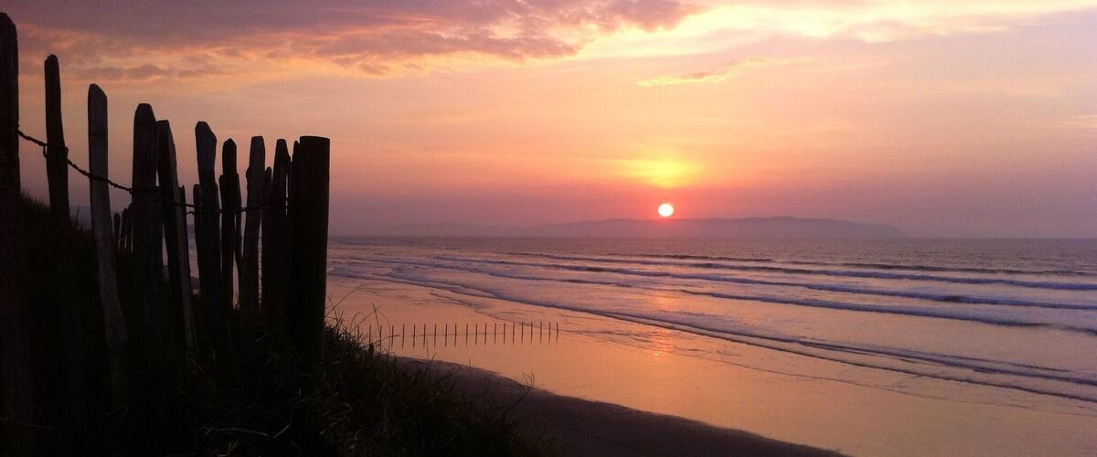 Un atardecer sobre una playa con una valla de madera al frente.