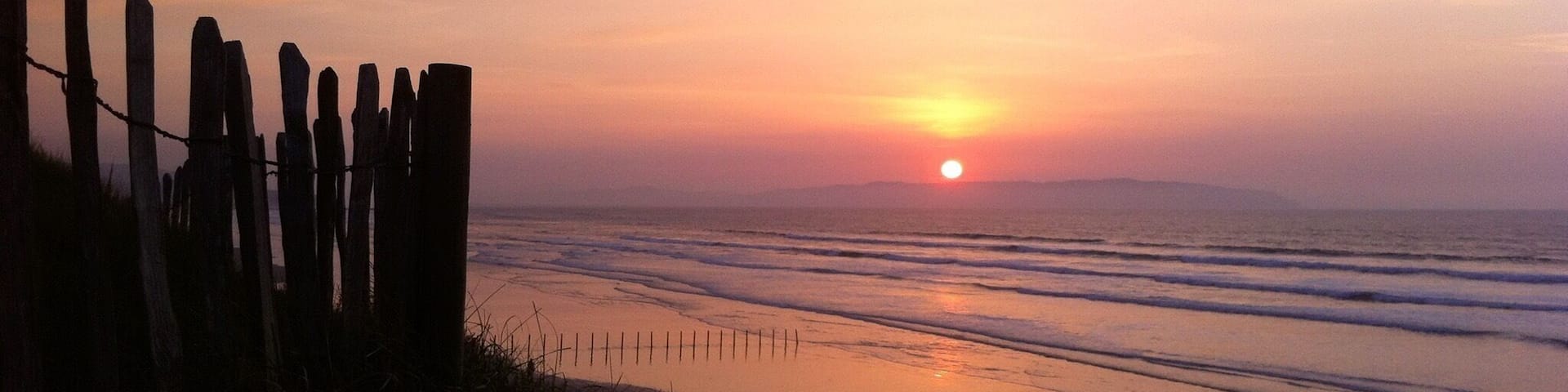A sunset over a beach with a wooden fence in the foreground.