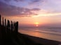 A sunset over a beach with a wooden fence in the foreground.