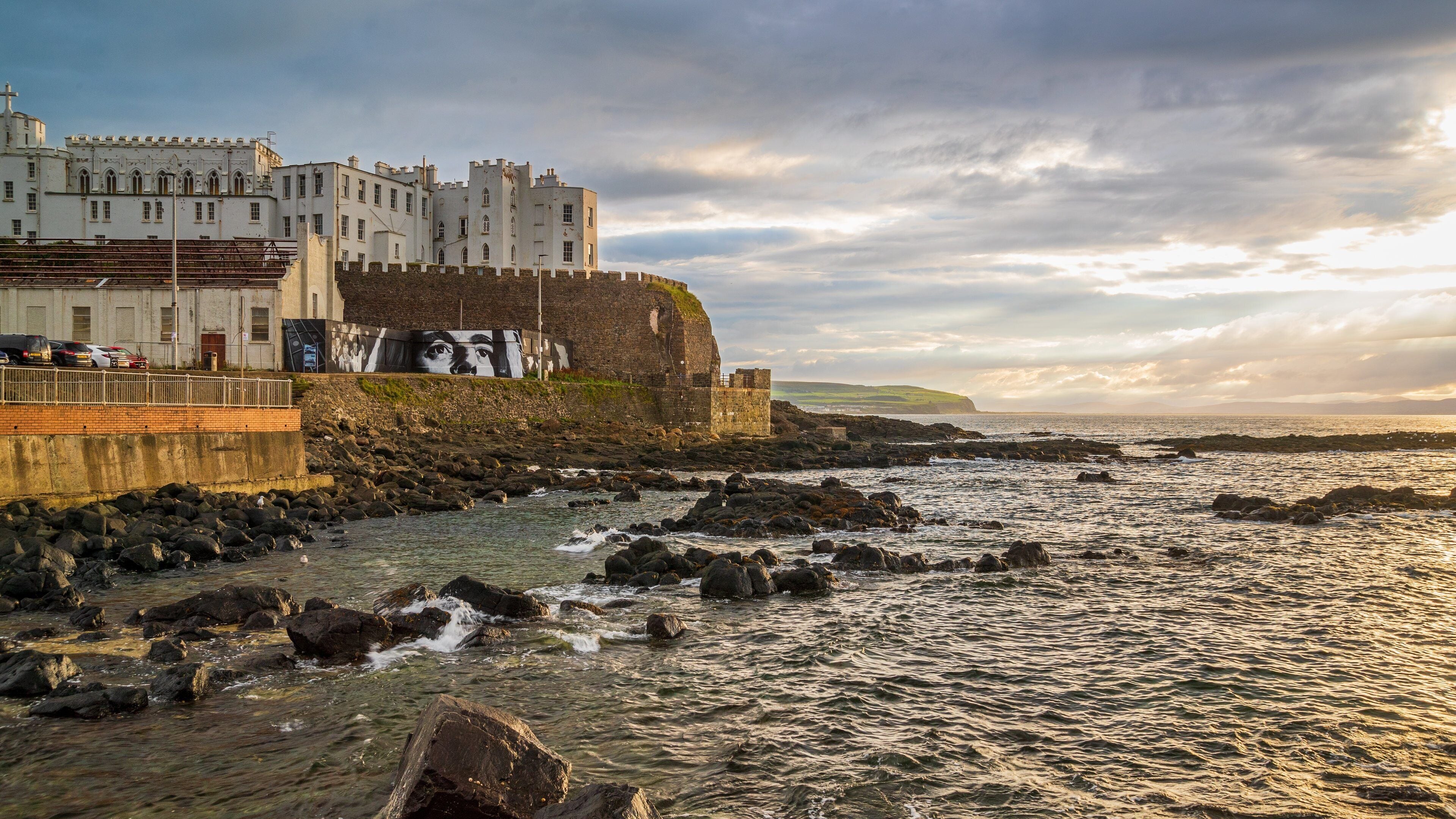 A coastal town with historic buildings, a rocky shoreline, and a mural on a wall.