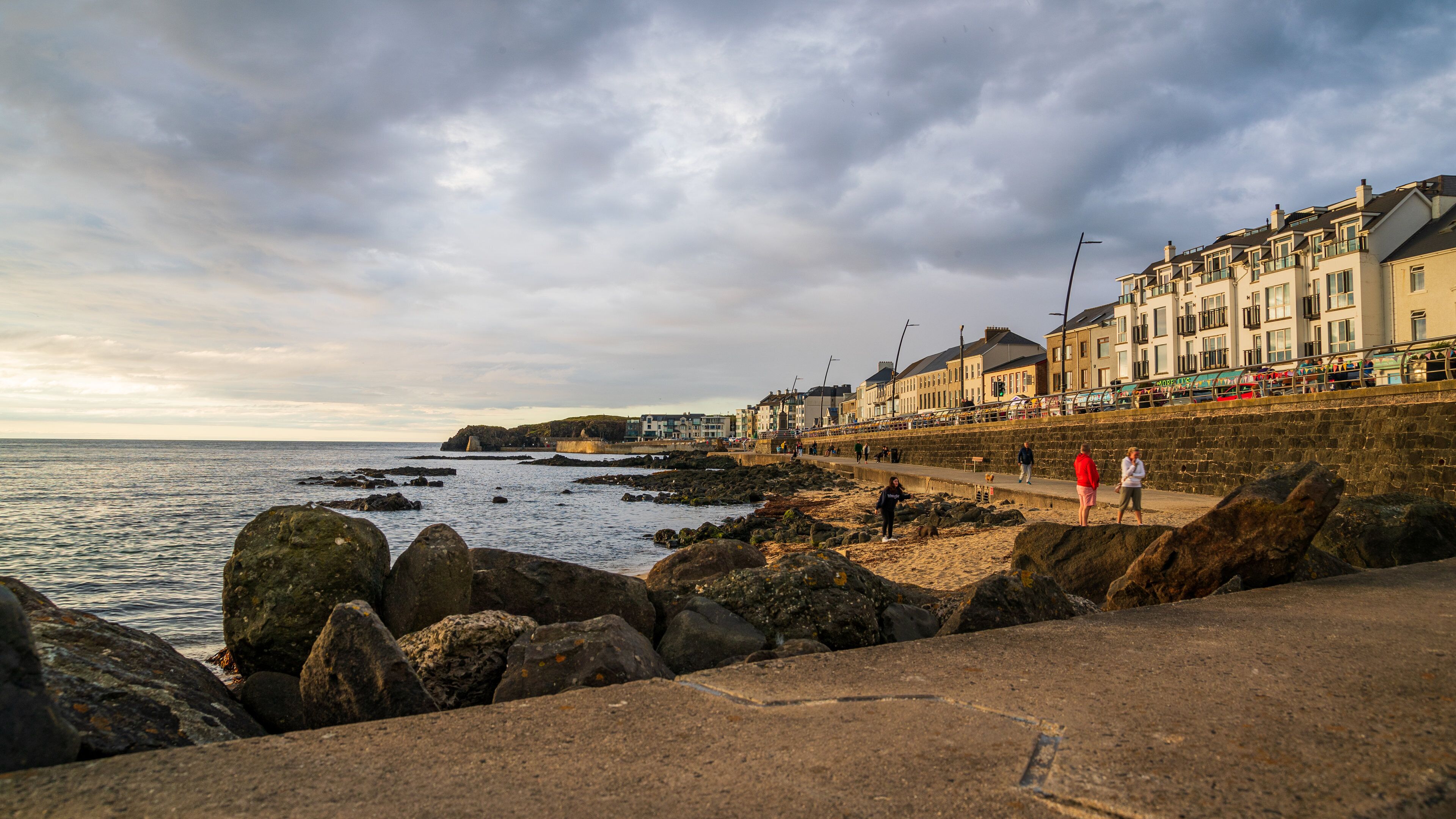 A rocky shoreline with a row of buildings along the coast.