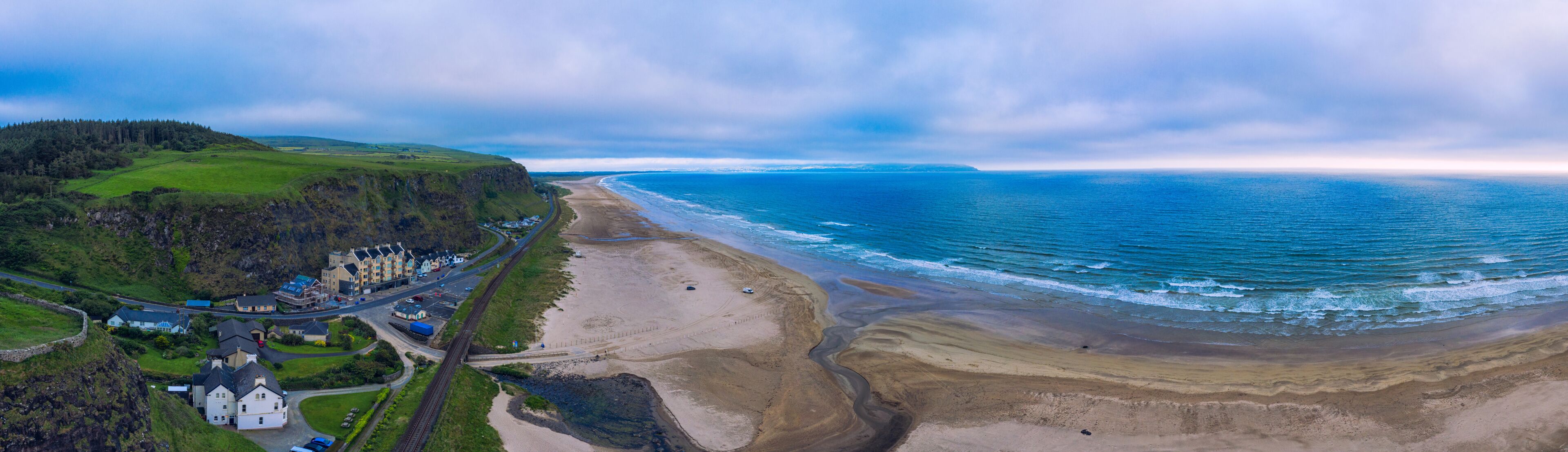 Paisagem costeira com praia, estrada e um conjunto de edifícios.