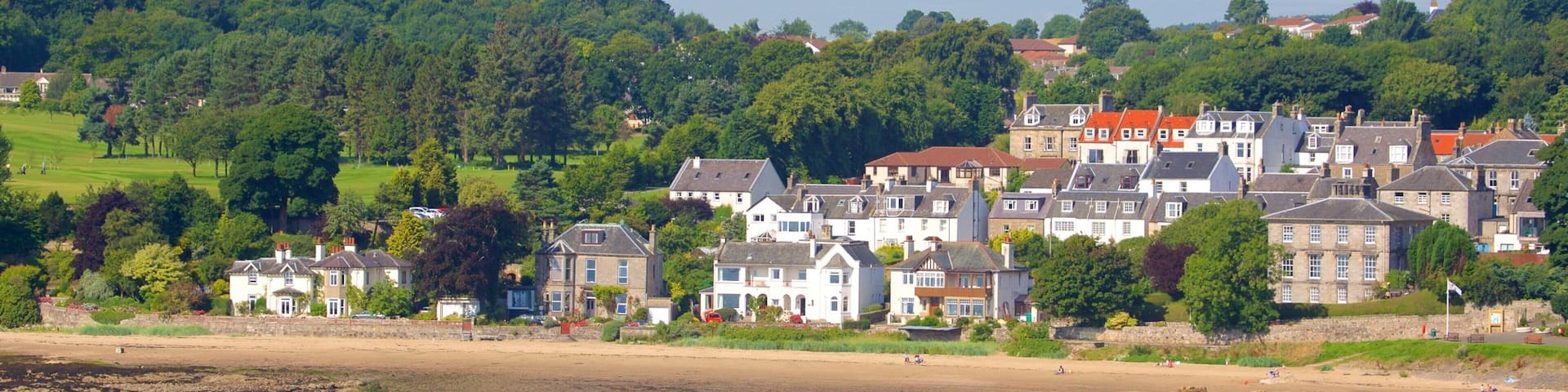A coastal town with historic buildings, a sandy beach, and a forested hill in the background.