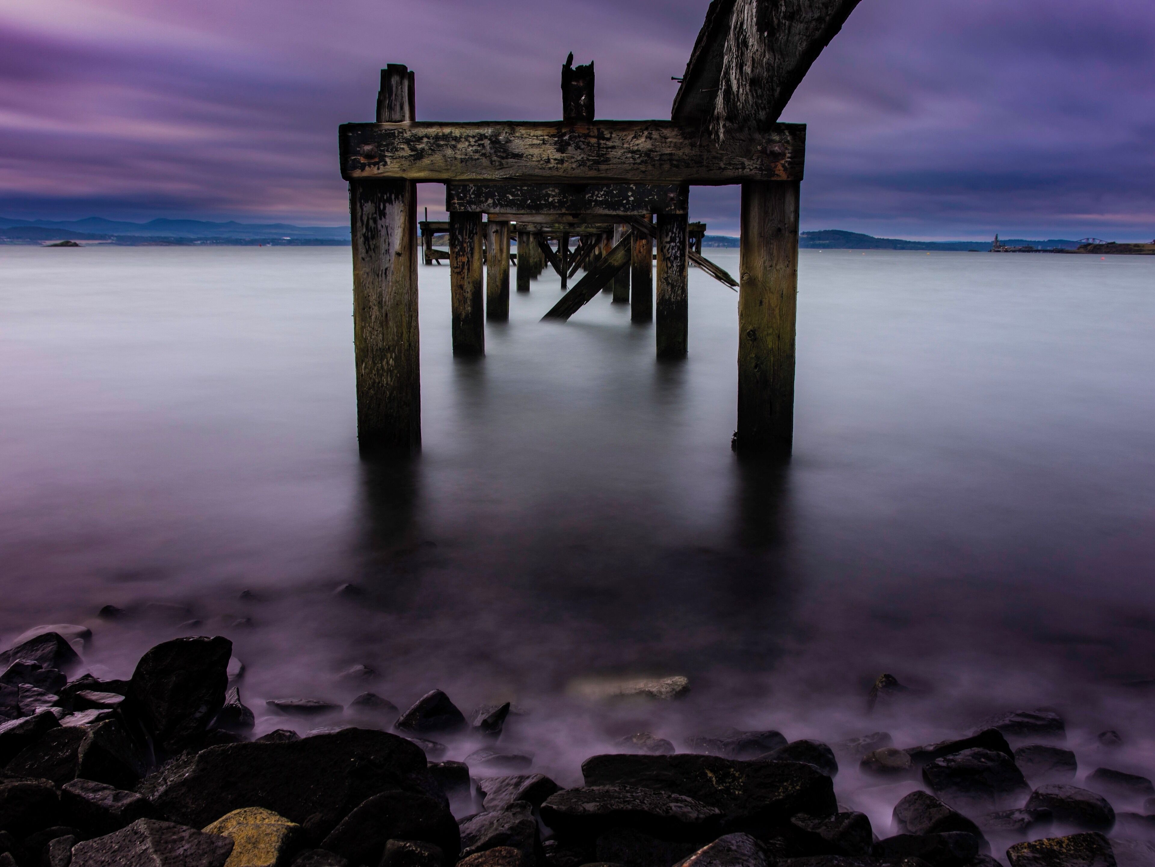 A wooden pier extending into calm waters with a purple sky.