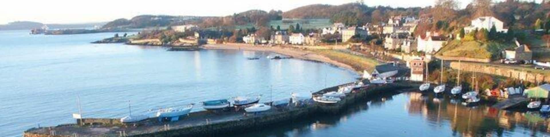 A coastal town with a long pier extending into calm waters, surrounded by houses and boats.
