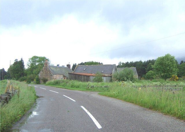 A rural road with stone buildings and lush greenery.